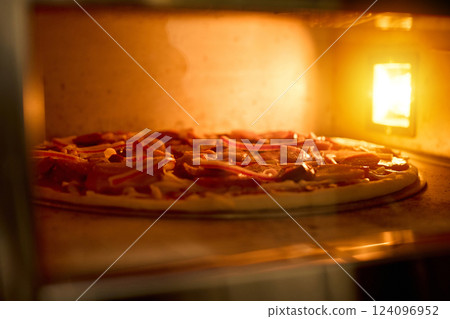 A delicious pizza is baking in an oven, showcasing vibrant toppings like peppers and meat. The warm glow from the oven lights up the kitchen as evening sets in A delicious pizza is baking in an oven, showcasing vibrant toppings like peppers and meat. The warm glow from the oven lights up the kitchen as evening sets in 124096952
