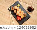 An appealing selection of sushi is arranged on a black slate plate, accompanied by chopsticks and small bowls of soy sauce, wasabi, and ginger 124096962