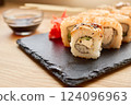 Delicious sushi rolls filled with fresh fish and vegetables are presented on a slate plate. Soy sauce and pickled ginger accompany the dish, enhancing flavors 124096963