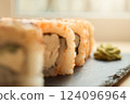 A beautifully arranged sushi roll sits on a slate plate, with a side of vibrant wasabi, showcasing the intricate details of the sushi and the freshness of the ingredients 124096964