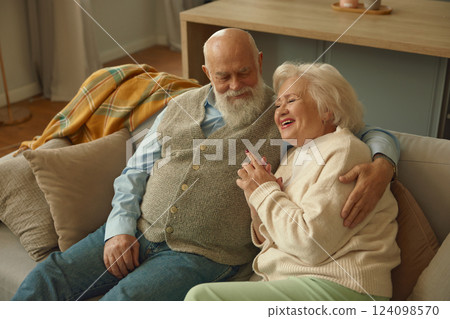 Smiling happy elderly couple feeling love and bonding hugging on sofa Smiling happy elderly couple feeling love and bonding hugging on sofa 124098570