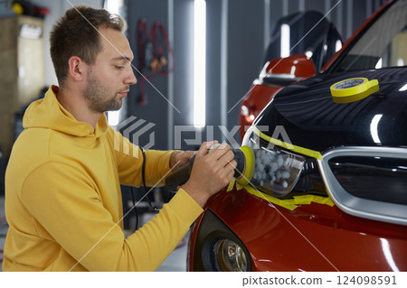 Man technician polishing headlamps at car garage workshop 124098591