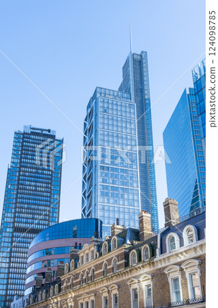 Skyscrapers stand tall against a clear blue sky in the City of London, showcasing modern architecture alongside historic buildings, creating a unique urban landscape. 124098785