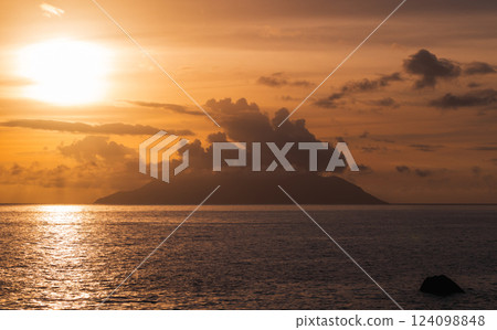 Golden sunset casting a serene glow over a calm sea with an island Golden sunset casting a serene glow over a calm sea with an island 124098848