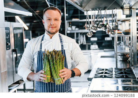 Man holding asparagus. Chef is on the kitchen preparing food Man holding asparagus. Chef is on the kitchen preparing food 124099188