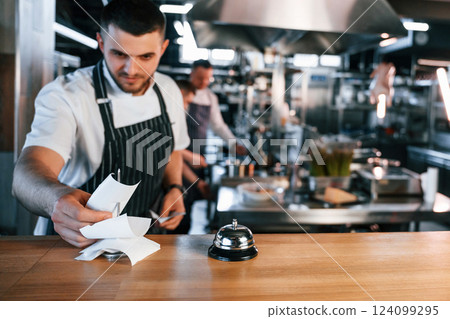Standing near the table with bell. Kitchen workers is together preparing the food Standing near the table with bell. Kitchen workers is together preparing the food 124099295