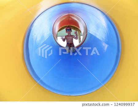 A cute little boy is getting ready to slide down a bright yellow plastic slide. Kid on the playground on the seashore on a warm summer day. little boy on a slide on the beach 124099937