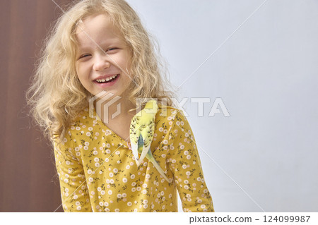 A laughing girl plays a budgie. The concept of friendship between children and pets. 124099987