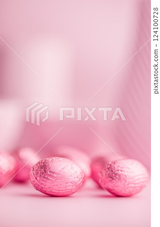 Chocolate easter eggs wrapped in pink colored foil on pink background. Chocolate easter eggs wrapped in pink colored foil on pink background. 124100728