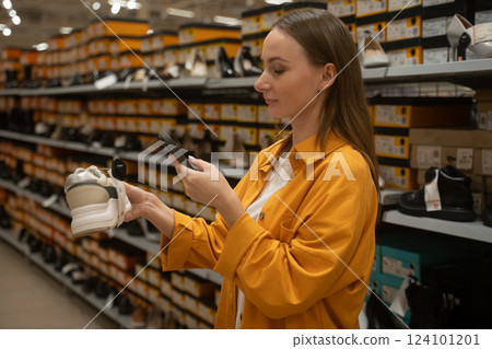 Woman scans shoes in retail store to check prices and availability during shopping trip in busy shopping aisle Woman scans shoes in retail store to check prices and availability during shopping trip in busy shopping aisle 124101201