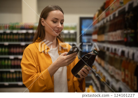Woman scans pomegranate juice in grocery store aisle during a shopping trip Woman scans pomegranate juice in grocery store aisle during a shopping trip 124101227