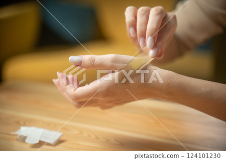 Applying a Band-Aid to treat a small cut on the arm while sitting at a wooden table 124101230