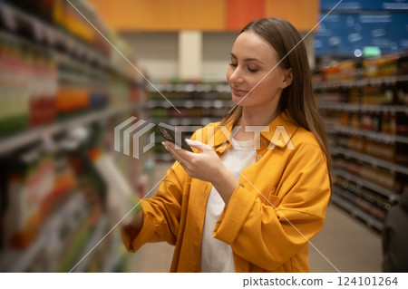Woman scans juice in supermarket aisle while shopping for healthy beverages during afternoon 124101264