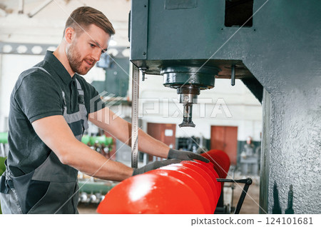 Measuring red colored sharp part. Man in uniform is in workstation developing details of agriculture technique Measuring red colored sharp part. Man in uniform is in workstation developing details of agriculture technique 124101681