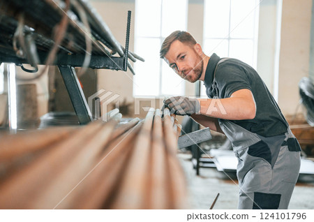Measuring lenght of metal pieces. Man in uniform is in workstation developing details of agriculture technique 124101796