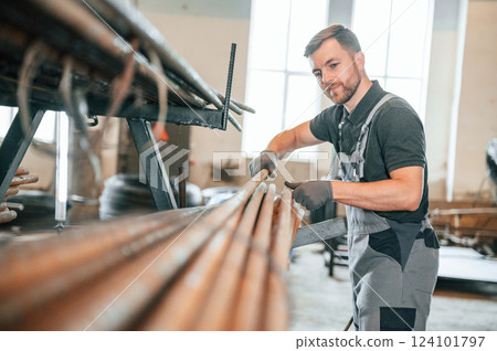 Measuring lenght of metal pieces. Man in uniform is in workstation developing details of agriculture technique Measuring lenght of metal pieces. Man in uniform is in workstation developing details of agriculture technique 124101797