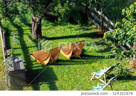 Above view wooden loungers rest under shady tree lush green lawn eco fresh open-air comfort. Relaxing backyard scene invites peaceful summer retreat orchard fence framing scenic hillside view 124101874