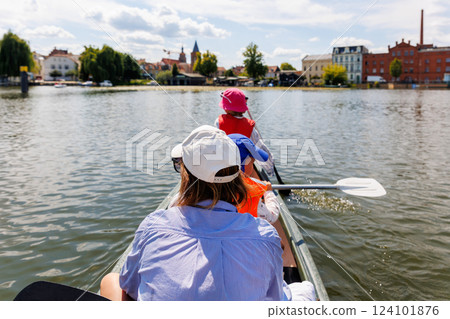Woman two children enjoy having fun paddling canoe rent across lake river water wearing bright orange life vests hot sunny summer day. Healthy recreational activity lifestyle vacation trip journey Woman two children enjoy having fun paddling canoe rent across lake river water wearing bright orange life vests hot sunny summer day. Healthy recreational activity lifestyle vacation trip journey 124101876