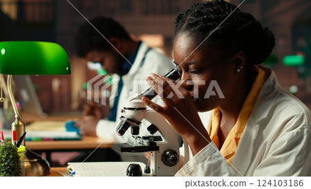 Female science student examines cells under the microscope for her scientific research in a campus library, takes notes about chemical processes and reactions for her thesis. Camera B. Female science student examines cells under the microscope for her scientific research in a campus library, takes notes about chemical processes and reactions for her thesis. Camera B. 124103186
