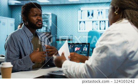 Medical consultation featuring a doctor advising a young man on diagnostics and treatment, utilizing radiology results and expert feedback in a facility. Clinical examination at cabinet. Camera B. 124103242