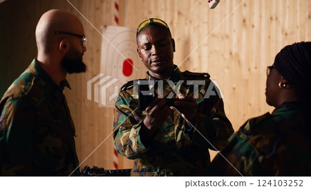 Army commander talking with recruits in shooting gallery, teaching them about weapons handling at close quarters. Military officer instructing soldiers, building combat habits, camera B 124103252