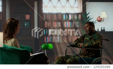 Wounded armed forces veteran in wheelchair discussing about war scenes, tells stories about horror of the combat. Distressed soldier with disability trying to recover with psychologist. Camera B. 124103260