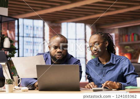 African American couple reviews their taxes and finances at home, using a calculator and laptop to track expenses, manage bills and plan their budget at home office. Financial responsibility. 124103362