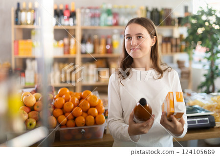Teenage girl choosing peach and tomato juices at grocery 124105689