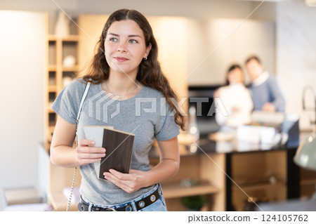 Female buyer with samples of material chooses kitchen set in furniture store Female buyer with samples of material chooses kitchen set in furniture store 124105762