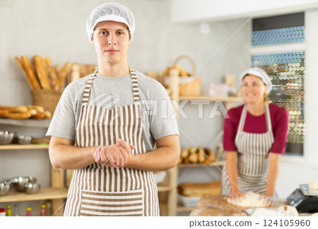 Portrait of young man baker smiling at camera posing during daily work in bakery 124105960