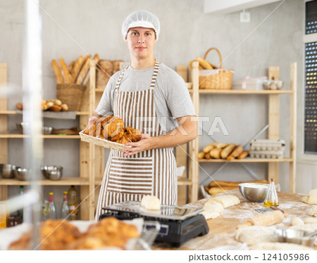 In working room of bakery, there is man with croissants in wicker basket in hands In working room of bakery, there is man with croissants in wicker basket in hands 124105986