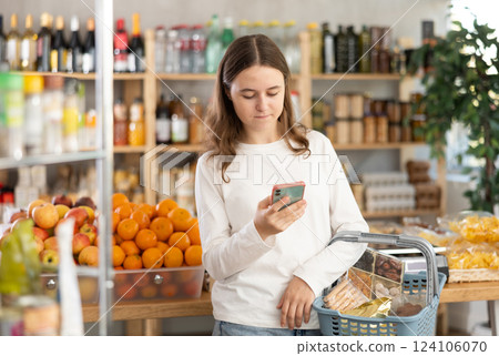 Teenage girl with phone choosing groceries in store 124106070