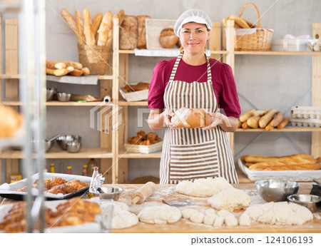 In working room of bakery, there is woman with loafs of bread in hands In working room of bakery, there is woman with loafs of bread in hands 124106193