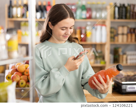 European teen girl customer at shop scans QR code on grapefruit juice bottle using phone camera European teen girl customer at shop scans QR code on grapefruit juice bottle using phone camera 124106221