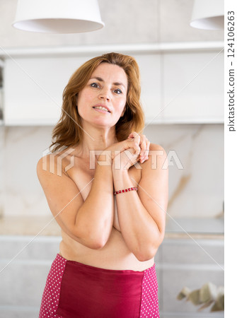 Standing topless woman with apron tied at waist covers bare chest with crossed arms Standing topless woman with apron tied at waist covers bare chest with crossed arms 124106263