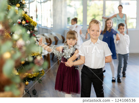 Group of preteen children in festive clothes dances waltz around Christmas tree 124106536