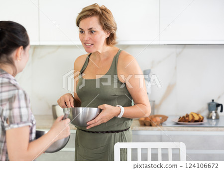 Middle-aged woman holding bowl talking to another woman in the kitchen 124106672