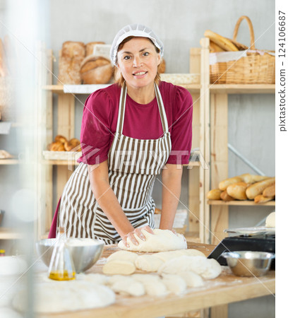 Adult female baker kneading dough on table 124106687