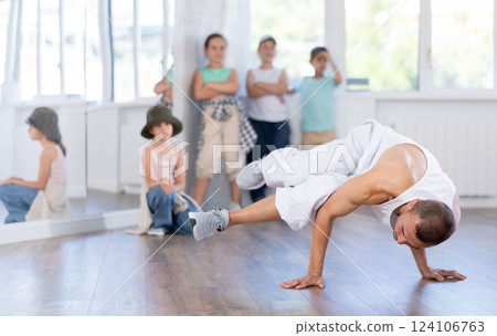Young male coach demonstrating to group of teen children hip hop dance moves in class Young male coach demonstrating to group of teen children hip hop dance moves in class 124106763