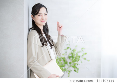 A beautiful woman in a suit with a laptop computer looks at the camera and gives a fist pump. For job changes, recruitment, human resources, consulting 124107445