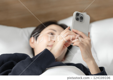 A woman watching a smartphone in bed 124109106