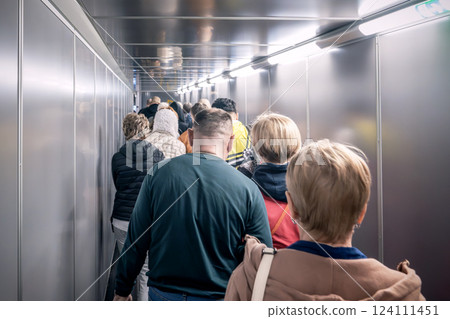People, passengers in a queue, walk along a telescopic ramp arm to board a flight. A busy and crowded airport boarding tunnel filled with numerous travelers eager to reach their flights. People, passengers in a queue, walk along a telescopic ramp arm to board a flight. A busy and crowded airport boarding tunnel filled with numerous travelers eager to reach their flights. 124111451