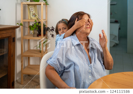 Girl covering grandmother eyes sitting on chair at 124111586