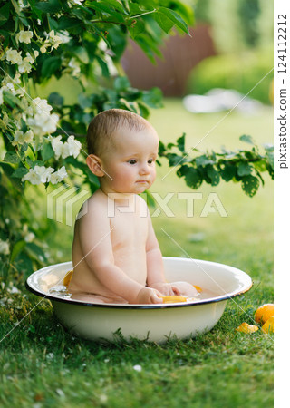 Baby Sitting In Outdoor Bath Tub With Fruit And Flowers 124112212