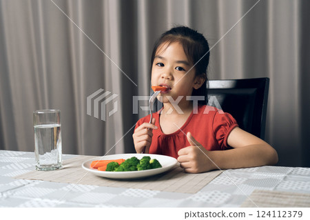Asian little girl eating healthy vegetables with relish. 124112379