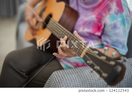 Person Playing Acoustic Guitar in Colorful Tie-Dye Shirt, Close-Up of Hands, Cozy Indoor Environment, Musician Focused on Performance 124112543
