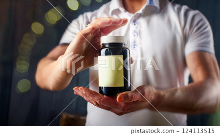 Hands holding a supplement bottle for energy with an empty label space for text. 124113515