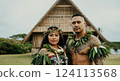 Traditional polynesian ceremony with couple in cultural attire outside ornate thatched structure 124113568