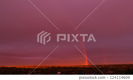 Faint rainbow arching across dramatic sunset sky over rooftops. 124114609