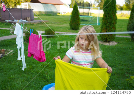 The backyard is peaceful as a young girl busily clips laundry, her golden hair catching the sunlight in soft waves. The backyard is peaceful as a young girl busily clips laundry, her golden hair catching the sunlight in soft waves. 124114790